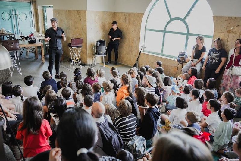 Decenas de niños y familias sentados en el suelo mirando a Sena