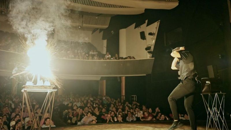 Sena en escena junto a una llamarada, frente a un teatro lleno